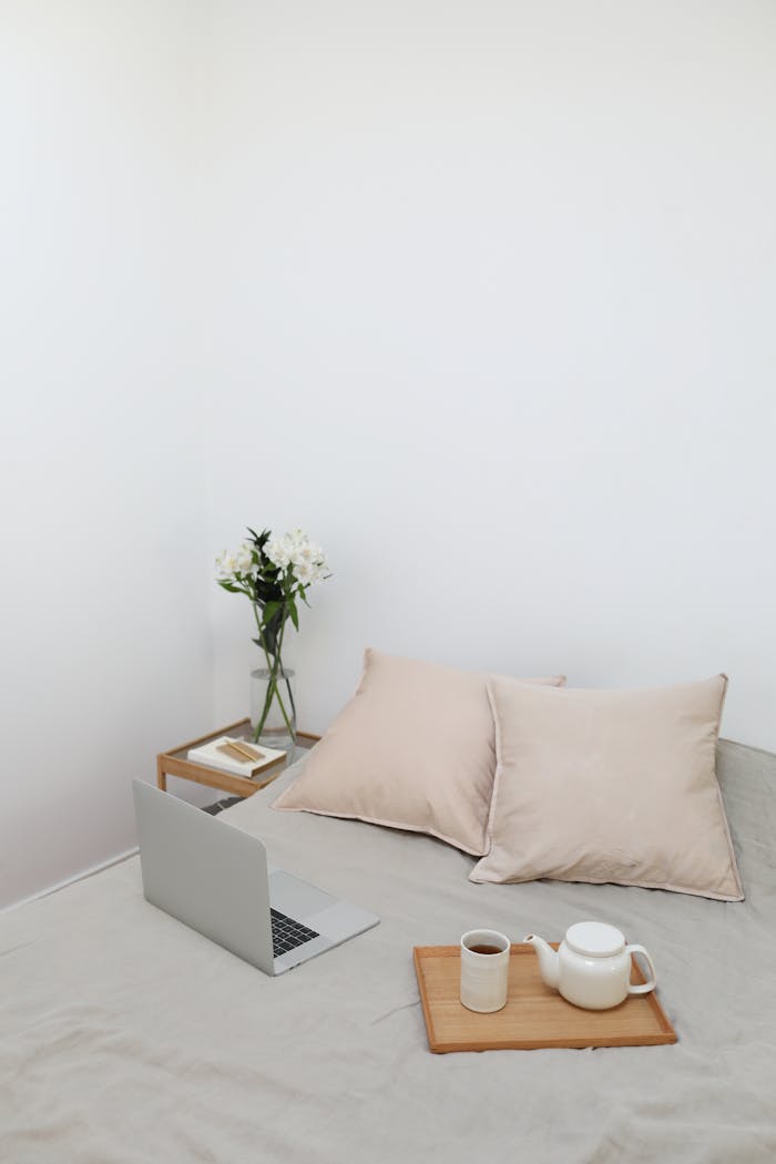 Minimalist bedroom setup with a laptop, coffee, and flowers, ideal for telecommuting.